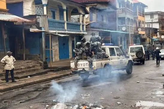 Security personnel patrol a Freetown street amid smoke following reported unrest.
